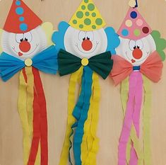 three paper clowns are hanging on the wall with streamers attached to them and one is wearing a party hat