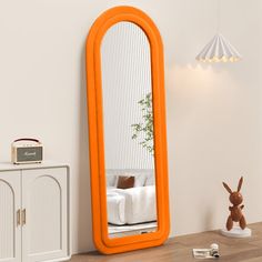 an orange mirror sitting on top of a wooden table next to a white cabinet and lamp