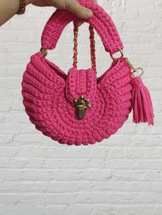 a hand holding a pink crocheted purse with tassels and gold hardware