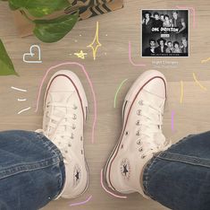 two pairs of white converse shoes sitting on top of a wooden floor next to a plant