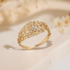 a gold ring sitting on top of a white table next to flowers and leaves with a diamond in the center