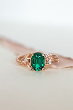 an emerald and diamond ring sitting on top of a white surface