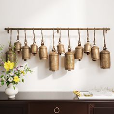 a bunch of bells hanging on a wall next to a vase with flowers in it