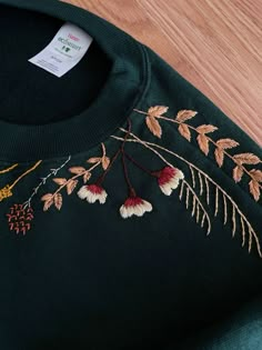 a green sweater with flowers and leaves embroidered on the front, sitting on a wooden floor