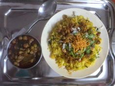 a white plate topped with rice and beans next to a bowl of chili sauce on a silver tray