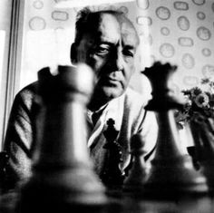 an old man sitting at a table with chess pieces in front of him and flowers