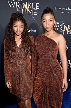 two women standing next to each other in front of a blue carpeted wall with the words wrinkle in time written on it