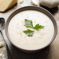 a bowl of soup with parsley in it and some cheese on the table next to it