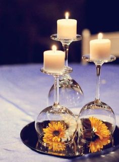 two wine glasses with sunflowers in them are sitting on a plate that is decorated with candles