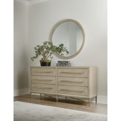 a plant is sitting on top of a dresser next to a round mirror and potted plant