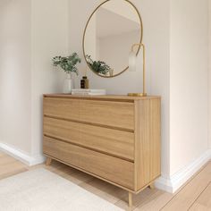 a wooden dresser with a round mirror on top and a potted plant in the corner