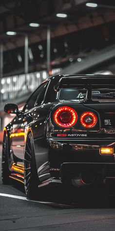 the rear end of a black sports car parked in a parking lot with other cars behind it