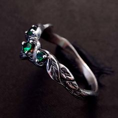 a silver ring with green stones and leaves on the side, sitting on a black surface