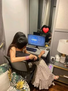 a woman sitting in front of a computer on top of a desk next to a lamp