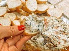 a hand holding a piece of bread with cheese on it and other food items in the background