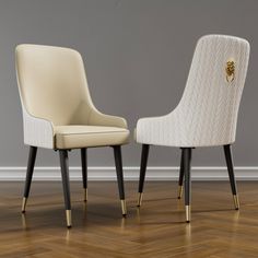 two white chairs sitting next to each other on top of a hard wood floor in front of a gray wall