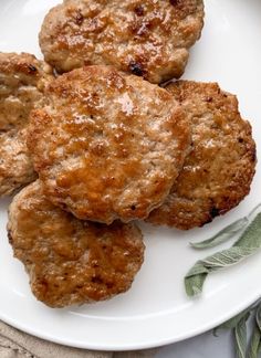 three hamburger patties on a white plate with sage sprigs and seasoning