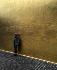 a man standing next to a gold wall