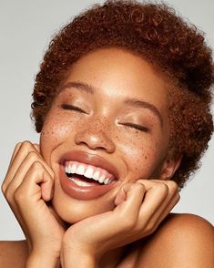 a woman with freckles on her face smiles and holds her hand to her chin