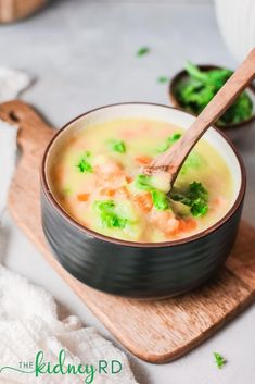 a bowl of soup with broccoli and carrots on a cutting board next to a wooden spoon