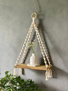 a white vase sitting on top of a wooden shelf next to a wall hanging planter