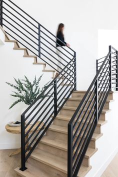 a woman is walking up the stairs in her home, with a plant on the floor