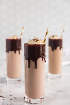 three glasses filled with chocolate milkshake and topped with whipped cream, toasted almonds, and drizzled with chocolate