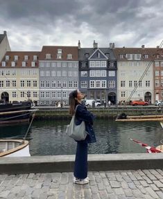 a woman standing on the edge of a pier looking at boats in the water and buildings behind her