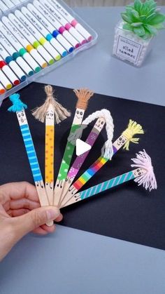 a person is holding up some colorful pencils on a table with markers and pens