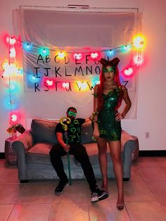 two people dressed up in costumes posing for the camera with neon lights on the wall behind them