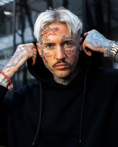 a man with white hair and tattoos on his face is holding his hands to his ears