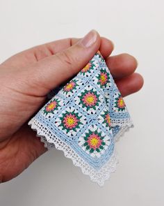 a hand is holding a piece of crocheted fabric with flowers on it,