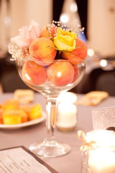 peaches and roses in a glass bowl on a table with candles, napkins and menu