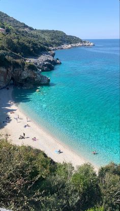 people are on the beach and in the water near some cliffs, with clear blue water