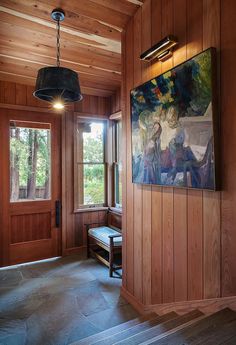 a room with wood paneling and a painting on the wall next to a bench