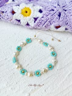 a bracelet with pearls and blue flowers on it next to a crocheted blanket