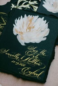 three black and gold wedding cards with white flowers on the front one is for each guest