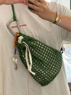 a person holding a cell phone in a green netted bag with keys attached to it