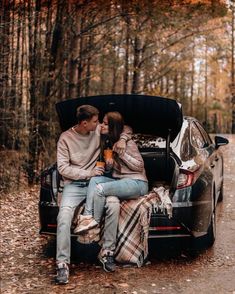 a man and woman sitting on the back of a car in the woods, kissing