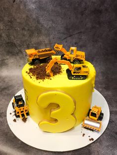 there is a yellow cake with construction trucks on it and the number 3 spelled out