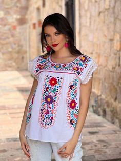 This Beautiful Hand embroidered blouse has a unique Mexican inspired Floral design and flirty lace sleeves. The blouse is a fresh cotton linen embroidered with cotton string. Paired with your favorite pair of jeans or a cute pair of shorts, the Floral Embroidered Elvira Top is a perfect addition to your wardrobe. This distinctive embroidery design originated in Puebla, Mexico. We have a deep appreciation for these beautiful works of art and the artisans who create them. With your help, we will s White Embroidered Cotton Lace Top, White Embroidered Short Sleeve Lace Top, White Embroidered Sleeve Summer Tops, White Bohemian Lace Top With Floral Embroidery, Multicolor Bohemian Blouse With Lace Trim, White Embroidered Top With Summer Lace Work, Bohemian Multicolor Lace Trim Blouse, White Embroidered Top With Lace Work For Summer, Festival Tops With Lace Trim And Short Sleeves