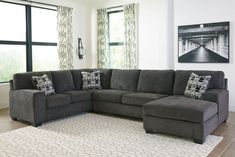 a living room with a large sectional couch and rug in front of two windows that look out onto the street