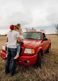 a man and woman standing on the hood of a red pick up truck in a field