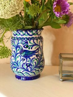 a blue and white vase with flowers on a table next to a small silver object