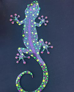 a lizard made out of beads on a black surface with green, purple and yellow dots