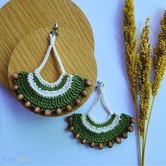 a pair of green and white crocheted earrings next to a wooden board with dried flowers