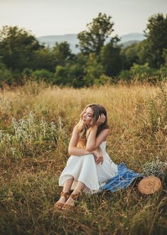 a woman sitting in the middle of a field with her head resting on her hand