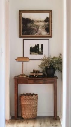 a wooden table topped with a lamp next to a painting and a basket filled with flowers