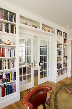 a living room filled with lots of books on top of white book shelves next to a red chair