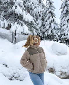 a woman standing in the snow with her hands on her hips and looking at trees